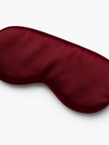 Jedwabna opaska na oczy Bordo Silk w bordowym kolorze, wykonana z naturalnego jedwabiu, ułożona na tkaninie – luksusowy dodatek do snu, szyty w Polsce.