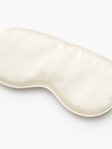 Jedwabna opaska na oczy Pearl Silk w perłowobiałym kolorze, elegancko ułożona na tkaninie – luksusowy dodatek do snu, uszyty w Polsce z naturalnego jedwabiu.